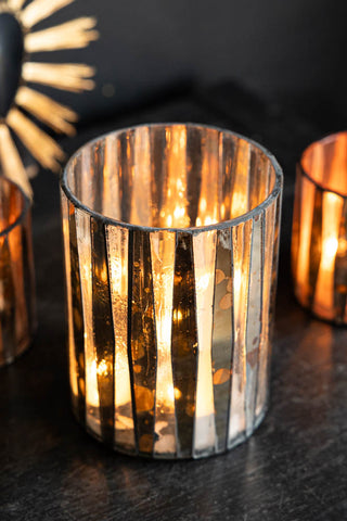 The Metallic Mosaic Effect Glass Candleholder with a lit candle inside, styled with smaller candleholders and an ornament inside.