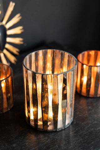 The Metallic Mosaic Effect Glass Candleholder styled on a black sideboard with other candle holders, with lit candles inside.