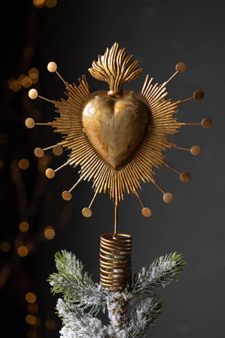 Image of the Milagro Heart Christmas Tree Topper styled on top of a christmas tree in front of a black wall.