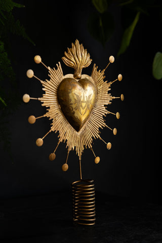 The Milagro Heart Christmas Tree Topper styled in front of a dark background with a plant.