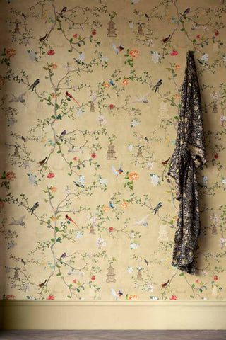 The Rockett St George Modern Chinoiserie Antique Gold Wallpaper on the wall with a patterned dressing gown hanging from the wall.