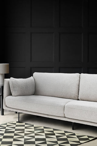 Close-up of the Modern Natural Boucle 3-Seater Sofa in a living room in front of a black panelled wall, styled with a monochrome rug, side table and a table lamp.