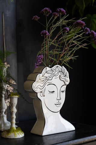 The Peaceful Monochrome Lady Vase seen from a side angle, displayed on a sideboard with some candlesticks and styled with flowers inside.