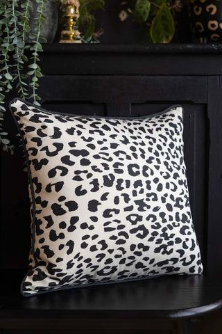 The Monochrome Leopard Cushion styled on a black bench with a sideboard and plants in the background