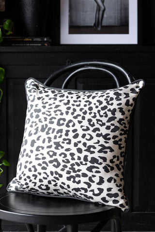 The Monochrome Leopard Cushion displayed on a black dining chair, styled with an art print, plant and other accessories in the background.