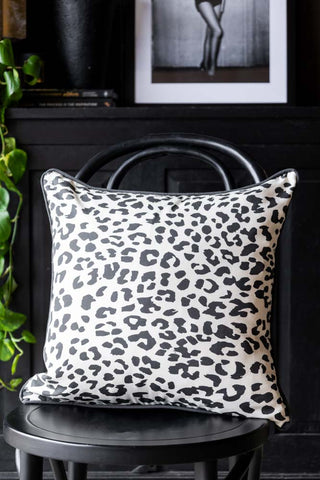 The Monochrome Leopard Cushion styled on a black chair with various accessories and a plant in the background.