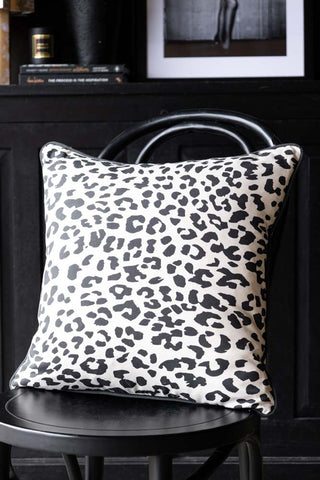 The reverse side of the Monochrome Leopard Sit The Fuck Down Cushion, displayed on a black dining chair.