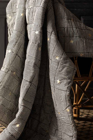 The Monochrome & Gold Star Detail Print Quilt in King-Size styled draped over a chair.