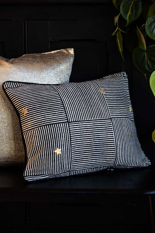 The Monochrome & Gold Star Print Cushion shown next to a gold cushion styled on a black bench.