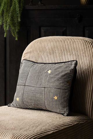 The Monochrome & Gold Star Print Cushion displayed on a chair.