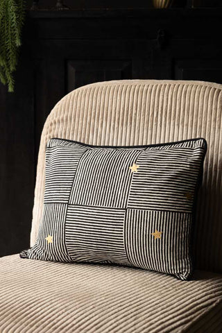 The Monochrome & Gold Star Print Cushion styled on a chair.