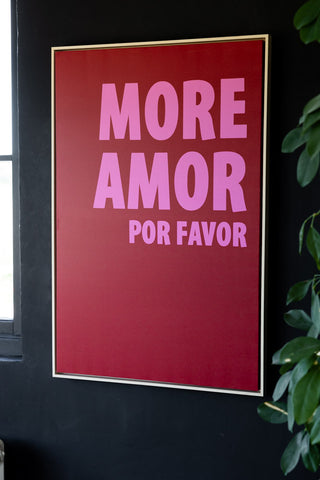 The More Amor Canvas styled on a black wall next to a plant and a window.