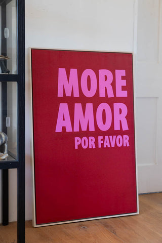 The More Amor Canvas styled on the floor leaning against a wall, next to a black display unit.