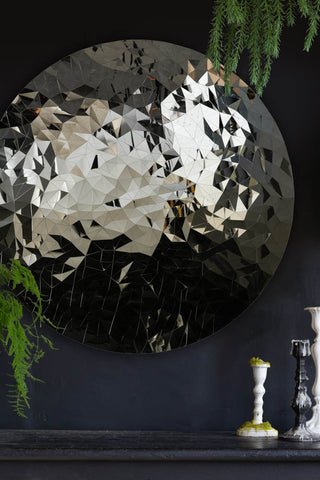 Detail shot of the Mosaic Disc Wall Art styled on a wall above a black sideboard and candlestick holders, surrounded with greenery.