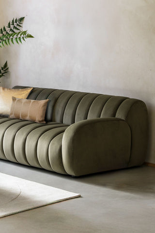 The Moss Green Roll Back 3-Seater Sofa styled in a neutral room, with some cushions, a rug and a plant.