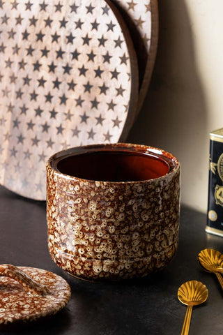 The Mottled Brown Lidded Pot with the lid off, styled on a dark table with some gold spoons, a tin and some wooden serving boards.