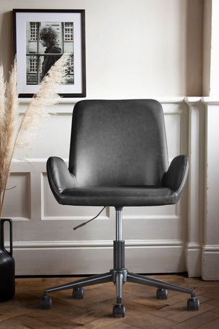 The Moulded Swivel Chair Charcoal styled in front of a white wall with a framed artwork and some dried grasses in a vase on the floor.