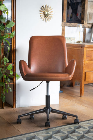 The Moulded Swivel Chair Mocha styled in front of a white wall, with various furniture, accessories and a plant in the background.