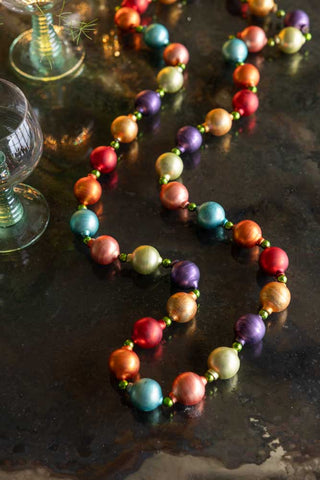 The Multi-Colour Bauble Garland displayed on a dark surface with some wine glasses. 