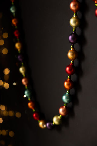 The Multi-Colour Bauble Garland styled on a dark surface, with some fairy lights in the background.