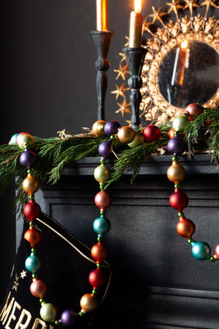 The Multi-Colour Bauble Garland hung over a black fireplace and a black and gold stocking.