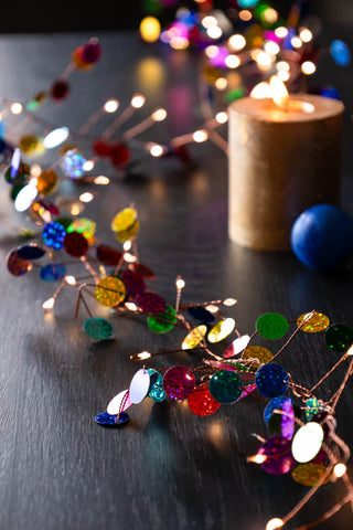 Close-up of the Multi Coloured Confetti Decorative Light Chain styled on a table amongst candles and decorations.