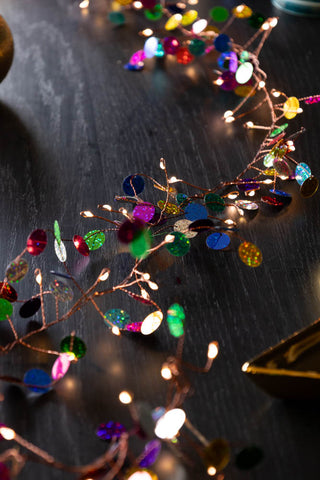 The Multi Coloured Confetti Decorative Light Chain styled on a dark wood table.