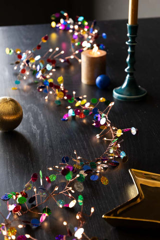 The Multi Coloured Confetti Decorative Light Chain styled on a dining table with tableware, candles and baubles.