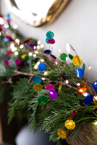 The Multi Coloured Confetti Decorative Light Chain styled on a mantlepiece with greenery