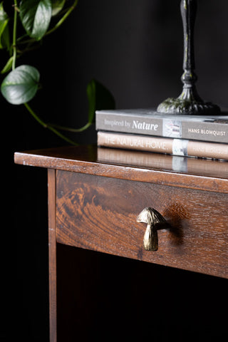 The Mushroom Knob - Gold displayed on a wooden drawer, styled with some books, a candlestick holder and a plant.