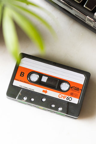 The My Favourite Tunes Cassette Tape Storage Tin seen from above, styled on a white surface with another storage tin and a plant.