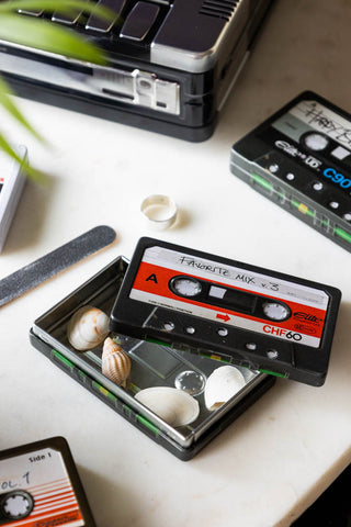 The My Favourite Tunes Cassette Tape Storage Tin styled with the lid off and various accessories inside/around it, on a surface with other similar storage tins.