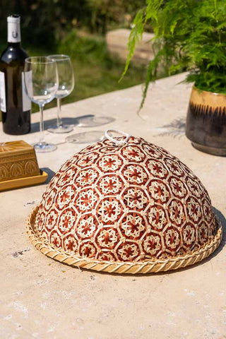 The Natural Bamboo & Red Floral Detail Food Cover styled on an outdoor table with a wine bottle, wine glasses, butter dish and plant.