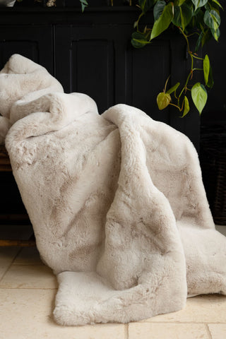 The Natural Faux Fur Throw draped across a bench, with some greenery in the background.