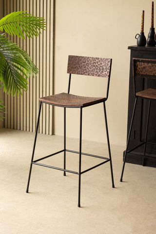 Two of the Natural Leopard Love Bar Stools displayed in front of a black sideboard, styled with candles and a plant.