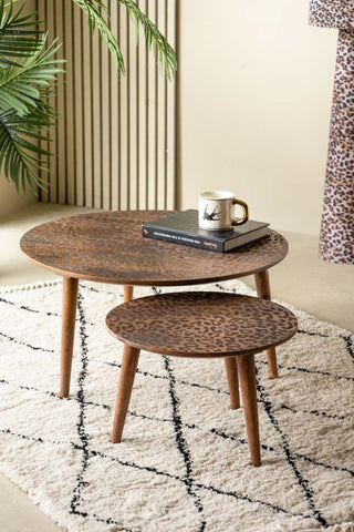 The Natural Leopard Love Nest Of Coffee Tables styled with a book and mug, displayed on a rug with a plant and a leopard print lamp in the background.
