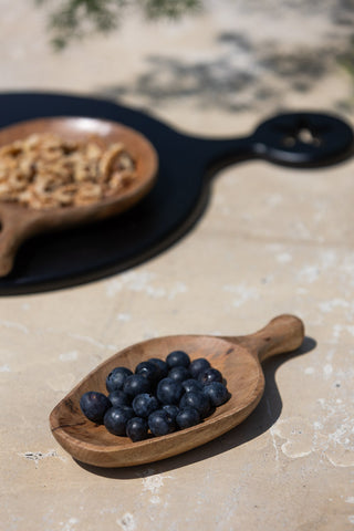 The Natural Wood Carved Serving Dish styled on a table with blueberries inside.