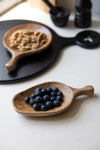 The Natural Wood Carved Serving Dish styled with berries inside, alongside the round version and various kitchen accessories.