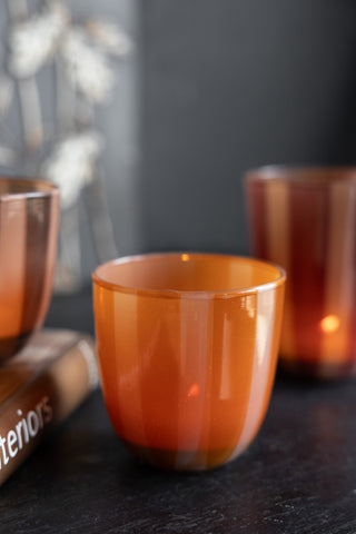 The Orange & Pink Tones Striped Tealight Holder - Short displayed on a dark surface with two other tealight holders and a book.