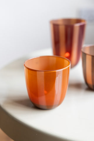 The Orange & Pink Tones Striped Tealight Holder - Short on a white round table with two other tealight holders in the background.