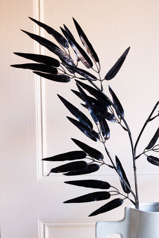 The Ornamental Bamboo In Black styled in a white vase in front of a neutral background.