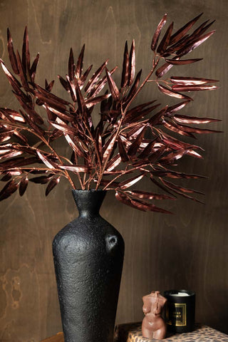 The Ornamental Bamboo In Bordeaux styled in a black vase, next to a leopard print book with some candles on the top.