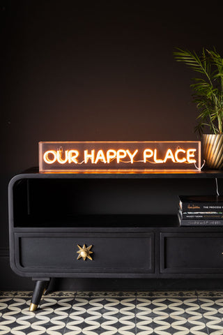 The Our Happy Place Neon Light Box styled on a black tv unit.