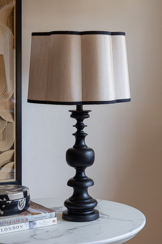 The Oyster Scalloped Easyfit Lampshade styled on a lamp base on a white marble table, along with a trinket box, some books and a piece of artwork on the wall.