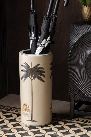 The Palm Tree, Royal Seal Inspired Printed Umbrella Stand with three umbrellas inside, styled on a geometric patterned floor next to a sideboard.