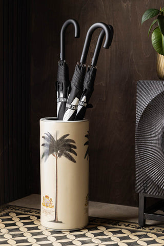 The Palm Tree, Royal Seal Inspired Printed Umbrella Stand styled with three umbrellas inside, next to a sideboard with a plant on.