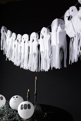 The Paper Ghost Halloween Garland hanging above a table, styled with lit candles, balloons and greenery.