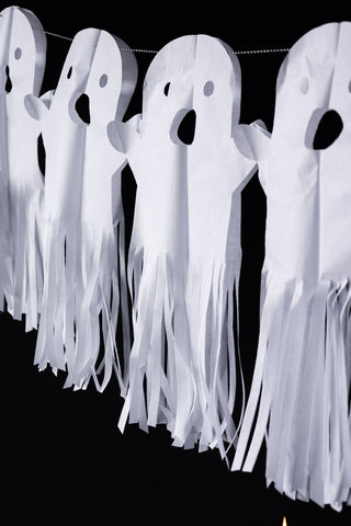 Close-up of the Paper Ghost Halloween Garland hanging in front of a black wall.