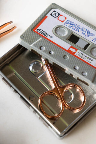 Close-up of the Party Mix Cassette Tape Storage Tin with some small scissors inside, with a pair of tweezers to the side of the shot.