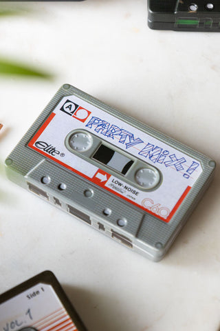 The Party Mix Cassette Tape Storage Tin styled on a white surface, with some other similar storage tins also in the shot.